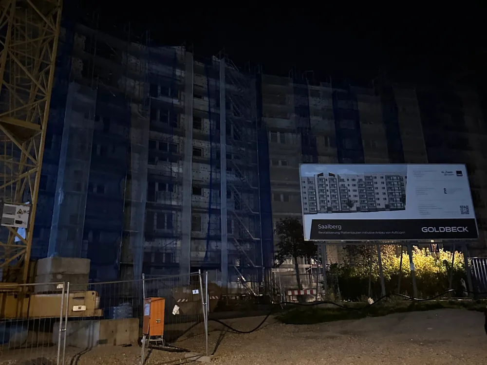 Baustelle Saalberg in Halle (Saale) bei Nacht: eingerüstete Wohnblöcke, Kran und Bauschild von Goldbeck zur Revitalisierung der Plattenbauten
